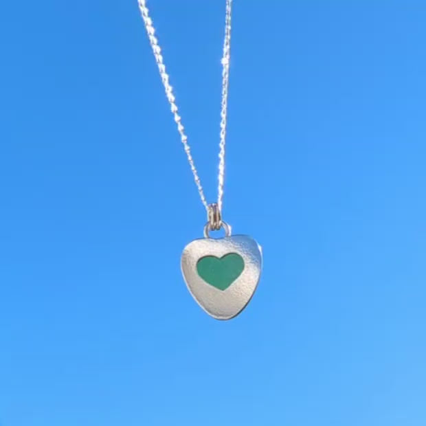 Video of Green Sea Glass silver pendant with heart shape cut out, with silver chain hanging with blue sky background.